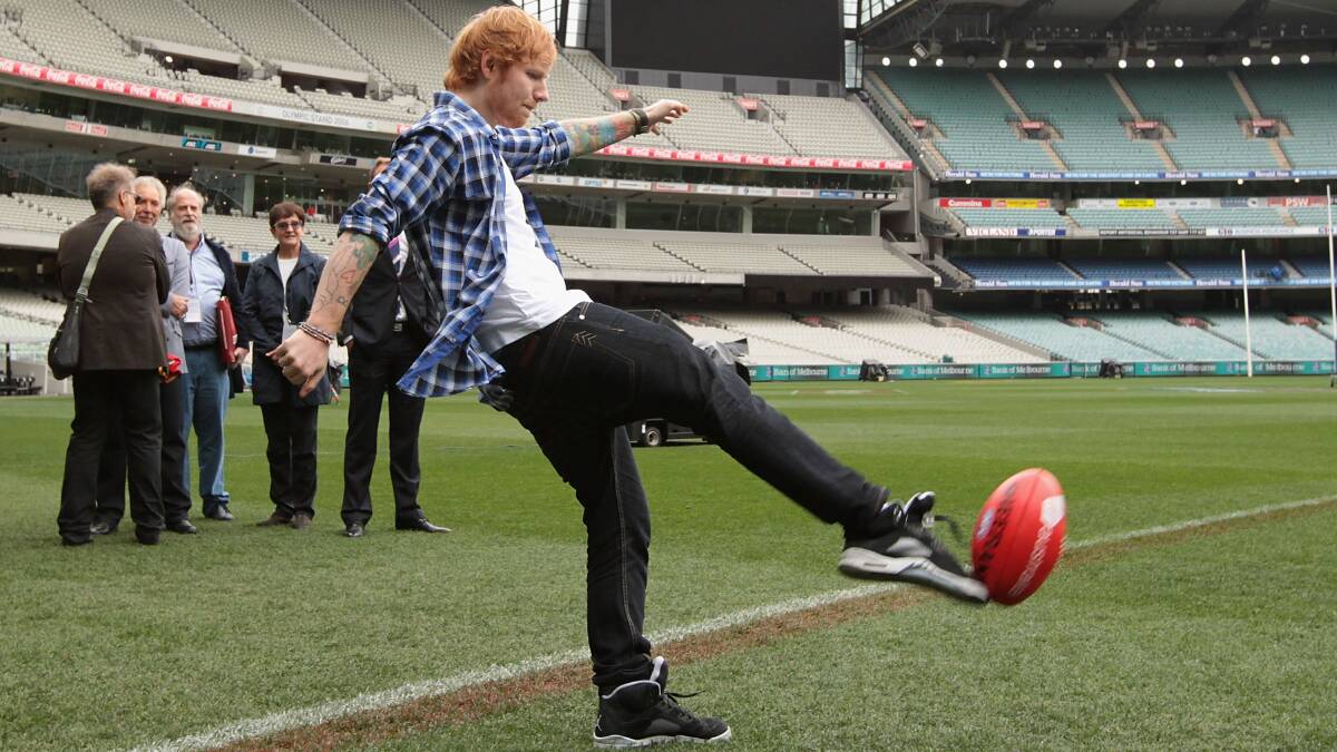 Ed Sheeran kicks a footy (in a flanno!) after a press conference before the 2014 AFL grand final. Picture: Getty Images