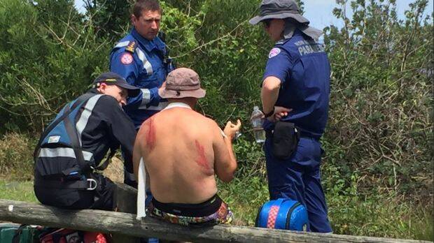 A man with a suspected broken collarbone speaks to paramedics after being washed off the rocks. Photo: Lachlan Leeming
