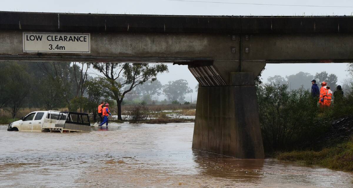 RISKY BUSINESS: Emergency service workers attend the scene of a vehicle stranded in floodwater on Minore Road. Photos: BELINDA SOOLE
