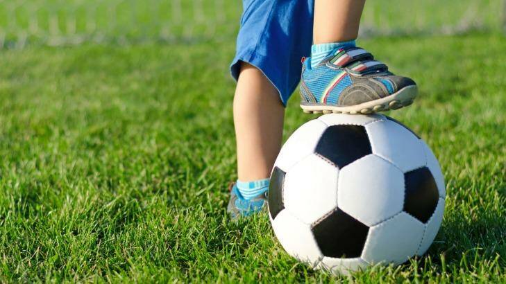 Little boy in shorts and trainers with his foot resting on top of a soccer ball on green grass with copyspace GENERIC soccer, sport field
