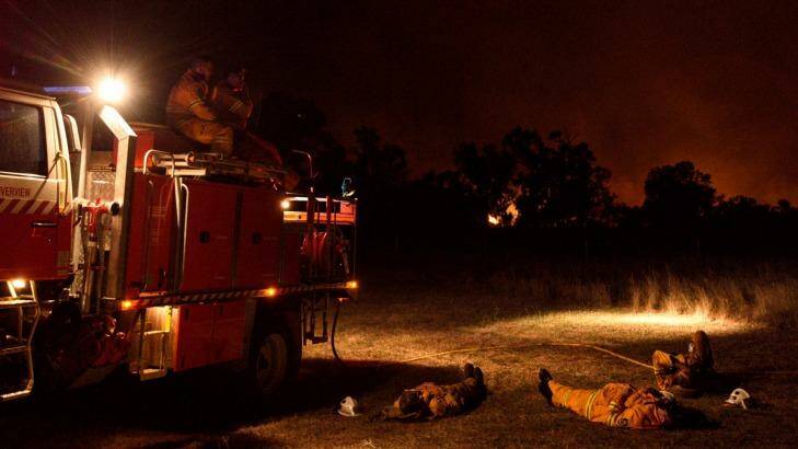 NSW RFS crew members from Cumberland Strike Team take a well earned rest after a long day of fighting a large grass fire burning towards the small township of Wollar in the greater Hunter region. Photo: Wolter Peeters