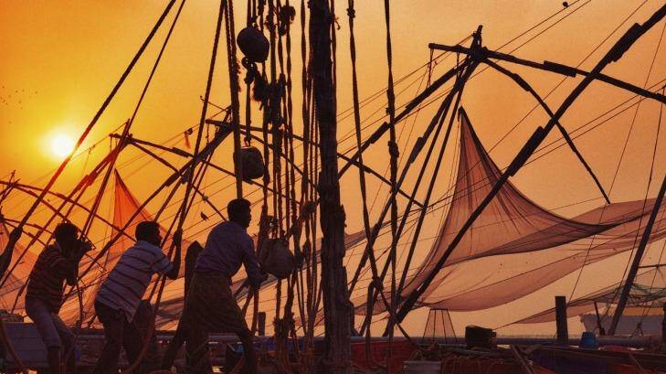 A crew hauls in a Chinese fishing net at sunset in Kochi, India.