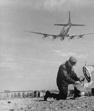 A technician mends the broken glass of a landing light at Tempelhof airport  as a Douglas C-54 Skymaster takes off during the Berlin Airlift, on April 25, 1949. Photo: H. William Tetlow/Keystone/Getty Images