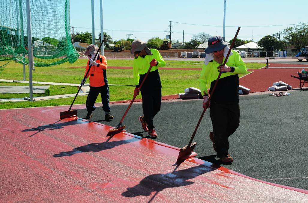 Workers Hew Kim, Kelvin Ting and Hew KC lay the surface of the running track at Barden Park. Photo: Greg Keen