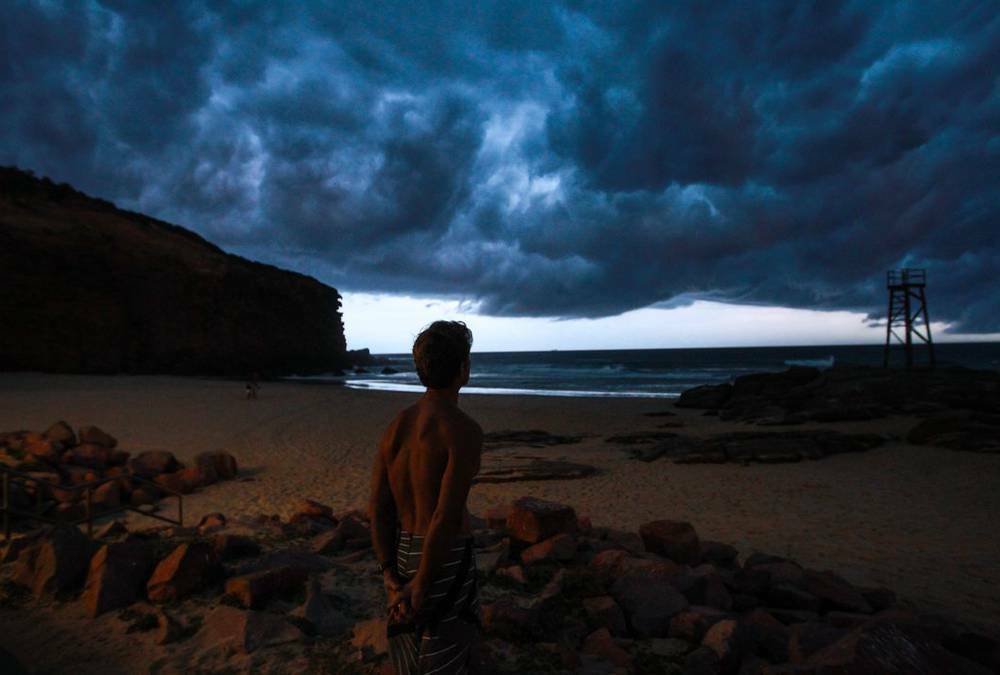 A beach-goer watches a developing storm roll in over Redhead Beach, causing high winds and heavy rain. Picture: Ryan Osland  