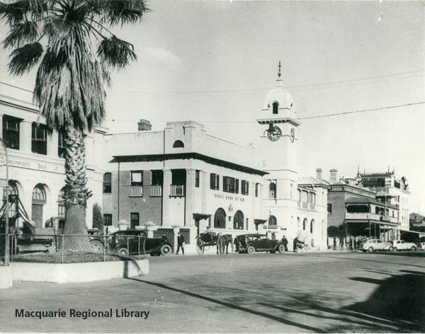 The eastern side of Macquarie Street in the 1940s. Severals cars and a horse and buggy are parked in the street. A fruit stall is located on the footpath. Image Macquarie Regional Library.