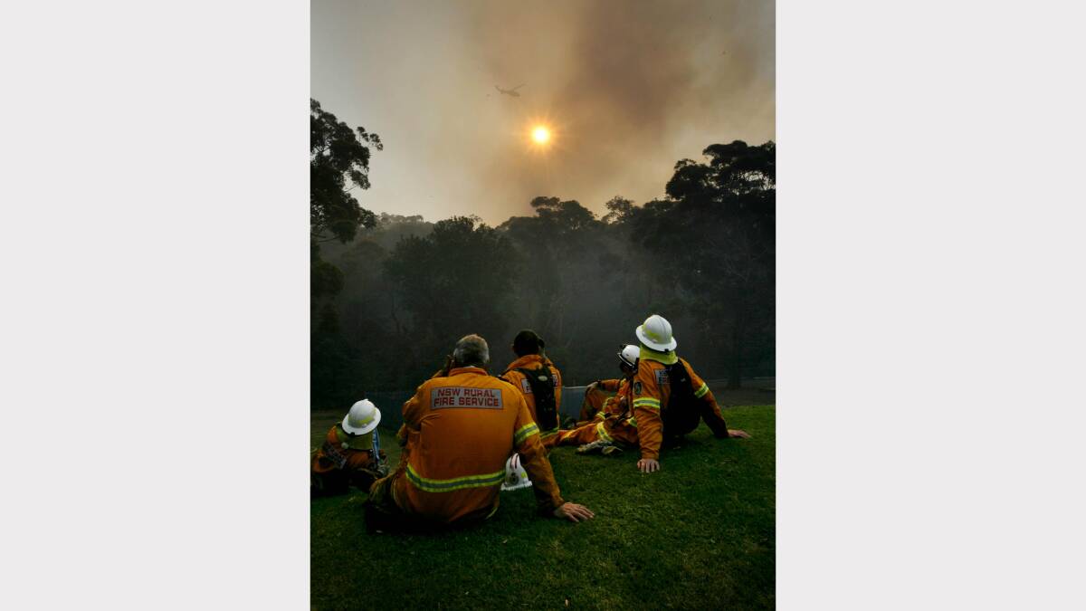  Image shows firefighters taking a break and watching a chopper firebomb at Dudley. Picture by  Darren Pateman