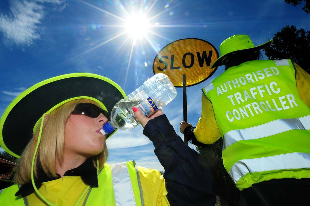Working safely in yesterday's top of 34 degree heat is Elaine Collins drinking water and Christine Kennedy holding the sign. Photo: LOUISE DONGES