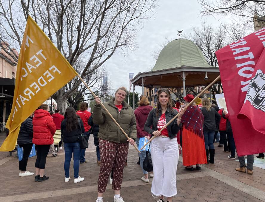 Two teachers holding banner flags for the NSW Teachers Federation (red) and Independent Education Union of Australia (yellow) at the protest march in Dubbo on 30 June 2022. Picture: Elizabeth Frias