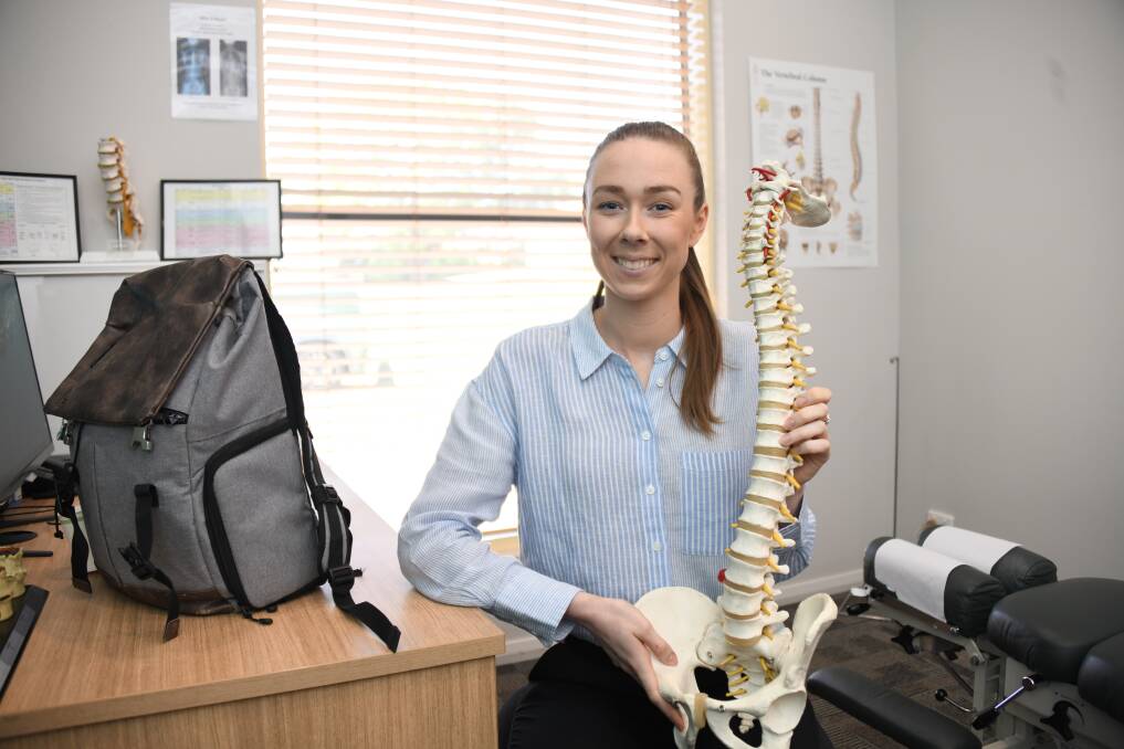 Chiropractor Madison Ryan next to a backpack and holding up a diarama of a spine. Picture by Amy McIntyre 
