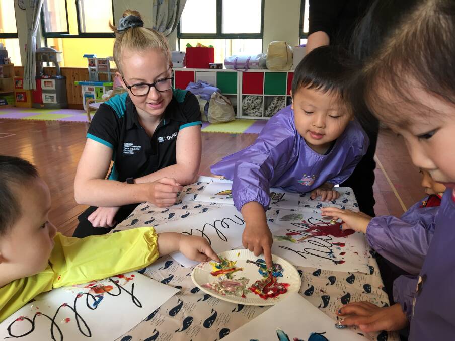 MESSY PLAY: Hannah Bass finger painting with the kids. “They teach more like school, it is very structured, whereas we teach by play in Australia,” she said.