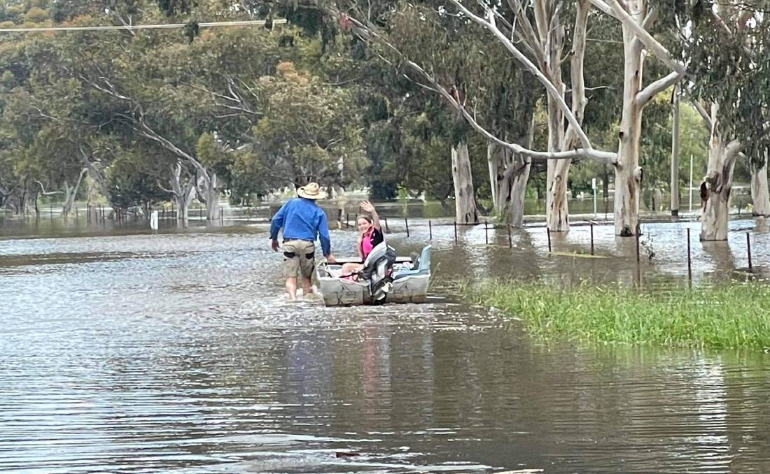 Sarah Price gives a wave as her father, Damien, drags the tinnie through flood waters at Forbes on the weekend. Picture supplied