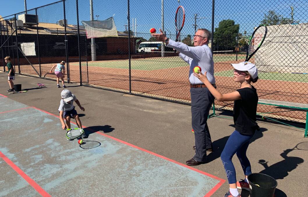 ACES: Parkes MP Mark Coulton tries his hand at serving at Paramount Tennis Club on Tuesday, while some local juniors assess his action. Photo: SUPPLIED