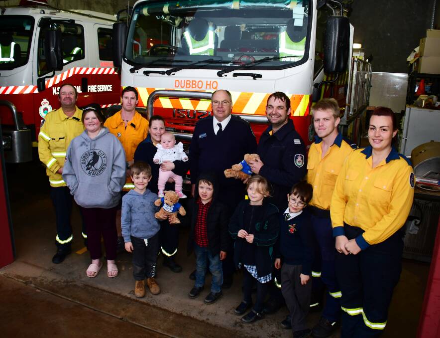 HELPING HAND: Orana RFS district service coordinator Mark Pickford handing the Gentle Bears over to the firefighter volunteers, pictured with their families. Photo: BELINDA SOOLE