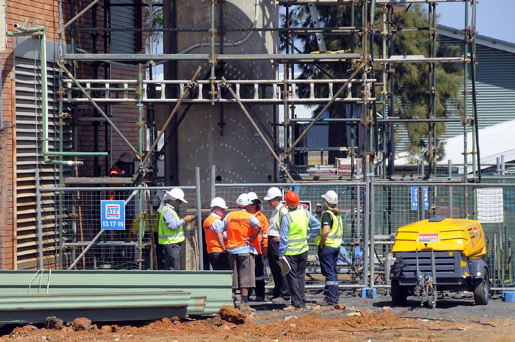 Workmen confer at the base of the 32-metre-high chimney stack that will make way for stage one and two redevelopment of Dubbo Base Hospital.