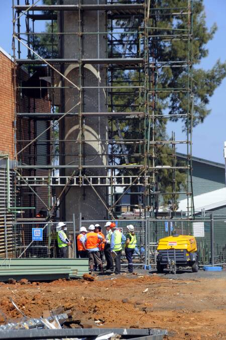 Workmen confer at the base of the 32-metre-high chimney stack that will make way for stage one and two redevelopment of Dubbo Base Hospital. Scaffolding has been erected around the structure in readiness for a start to its hands-on demolition this month. Photo: BELINDA SOOLE.
